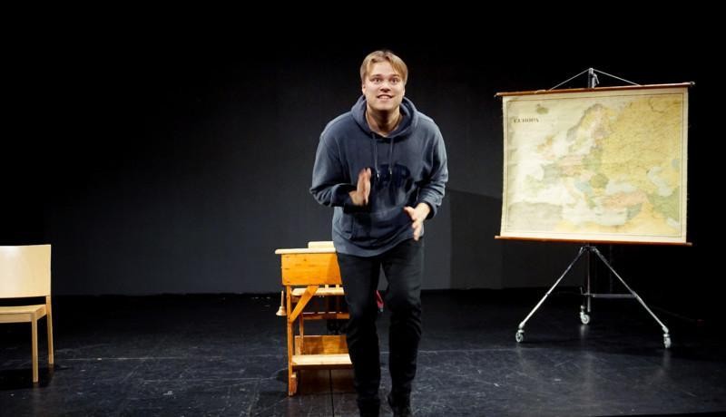 Skådespelare gestikulerar på en scen. Bakom honom syns en pulpet i trä och en gammal karta över Europa.