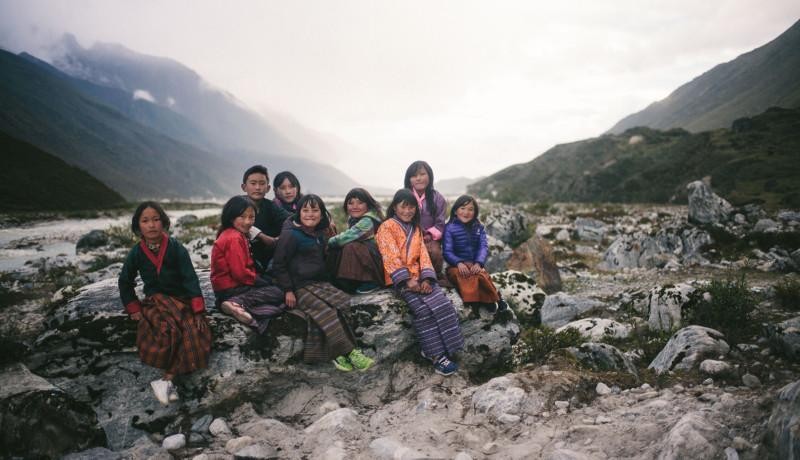 Nio barn i färggranna kläder sitter på stenar i ett dimmigt bergslandskap