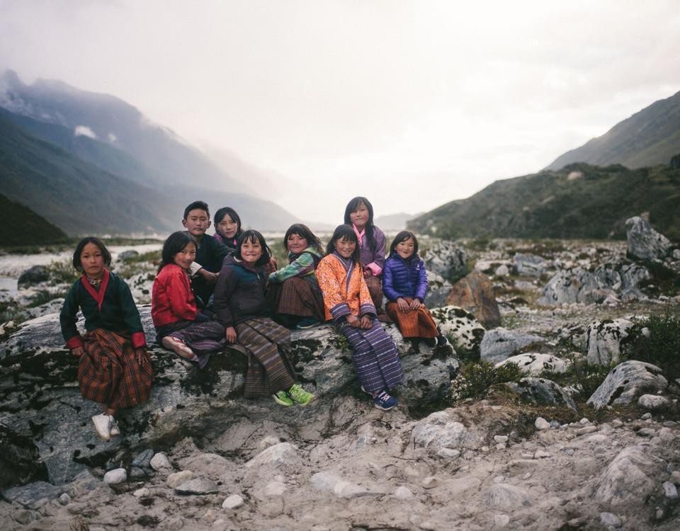 Nio barn i färggranna kläder sitter på stenar i ett dimmigt bergslandskap