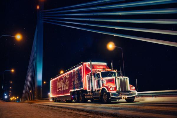 Gammaldags röd långtradare med Coca-Colas logotyp kör över en bro i mörkret.