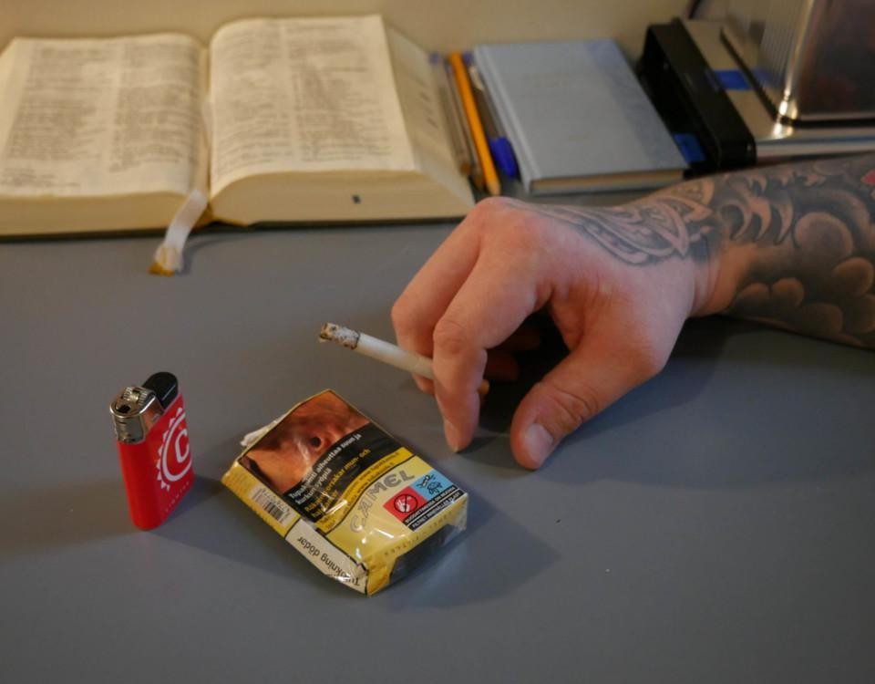 En hand håller i en cigarett ovanför ett ett cigarettpaket