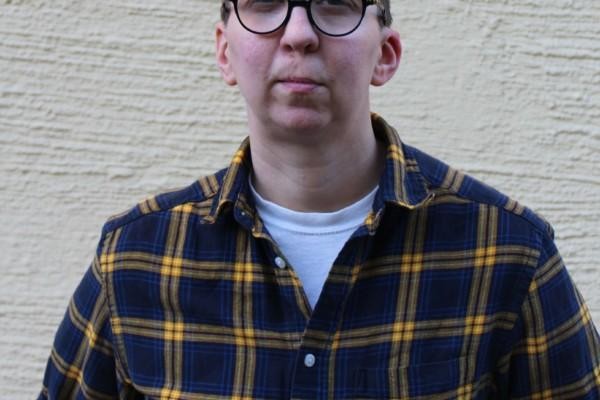 Porträttbild av en korthårig person med glasögon och rutig skjorta.