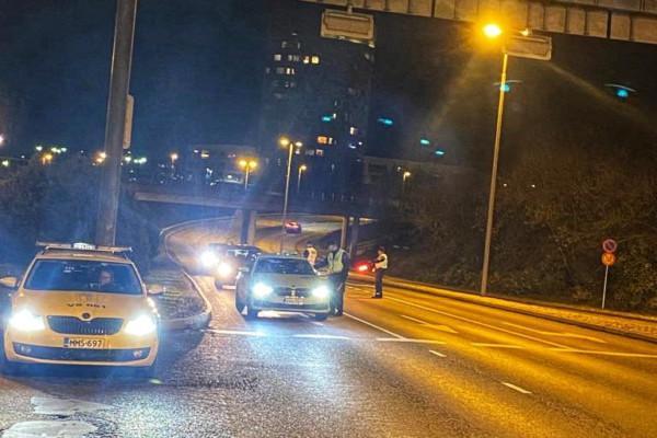 Flerfilig väg kvällstid. En polisbil står till vänster i bilden och tre personer står på körfältet bland personbilar.