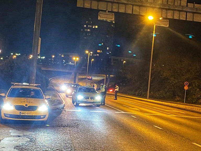 Flerfilig väg kvällstid. En polisbil står till vänster i bilden och tre personer står på körfältet bland personbilar.