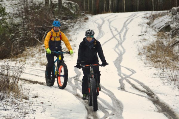 Två cyklister cykar på snöklädd skogsväg
