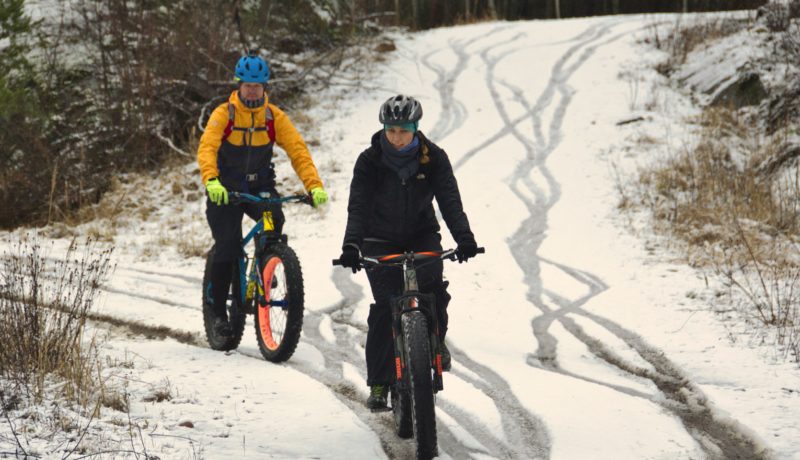 Två cyklister cykar på snöklädd skogsväg