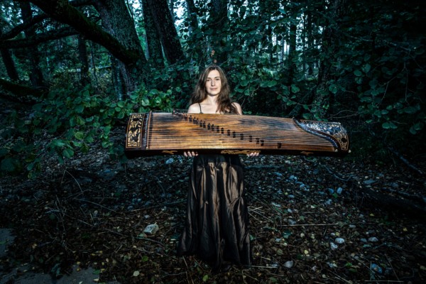 en kvinna i skogsmiljö med ett stort instrument i trä