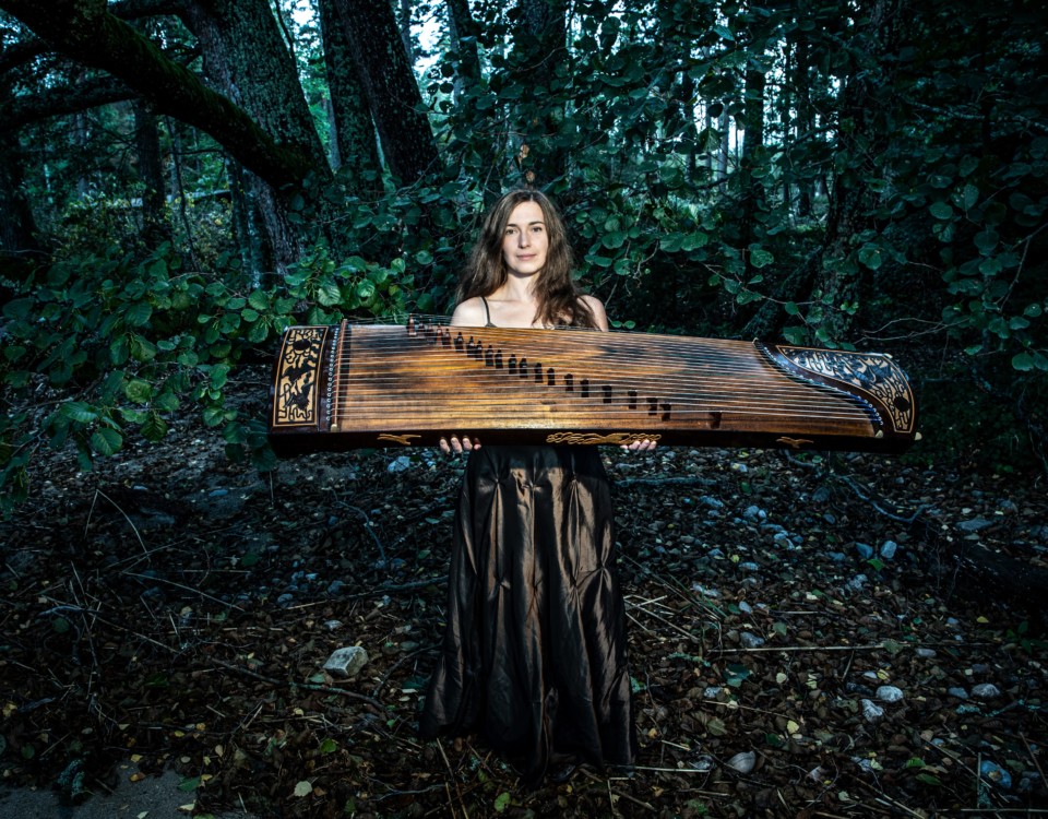 en kvinna i skogsmiljö med ett stort instrument i trä