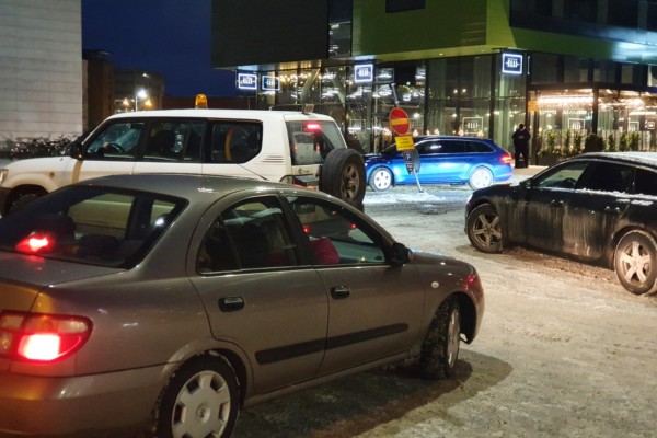 En parkeringsplats i vintermörkret där bilar kör åt olika håll.