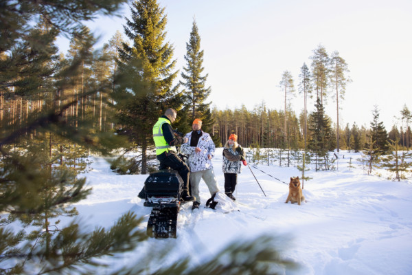 En inspektör iklädd reflexväst inspekterar en jägare. En flicka och en hund står bredvid dem i den snötäckta skogsgläntan.