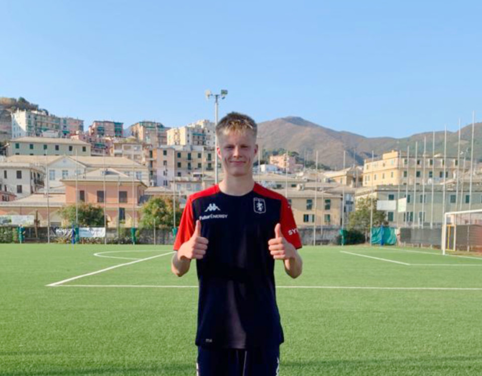 en ung man står vid en fotbollsplan och visar tummen upp