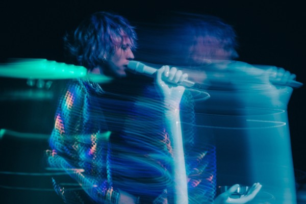 Artistbild i blått sken på en gitarrspelande sångare.