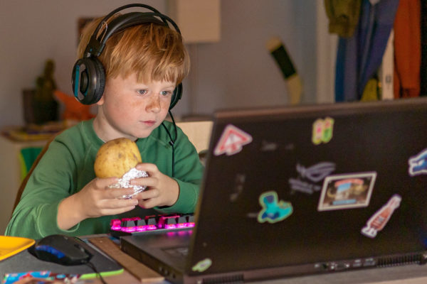 Rödhårig pojke med stor potatis i händerna tittar på en bärbar dator