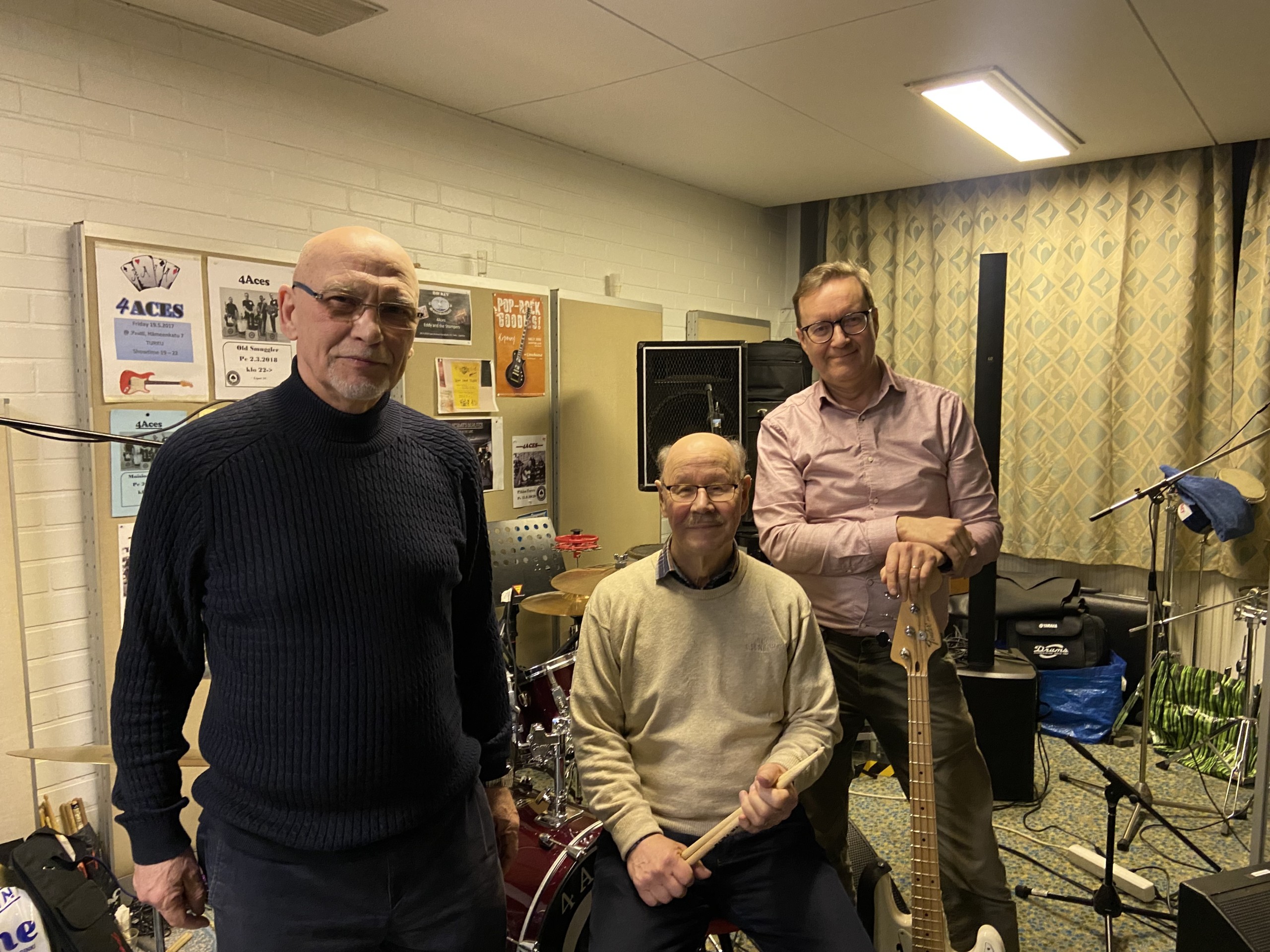 Tre män står och sitter med instrument.