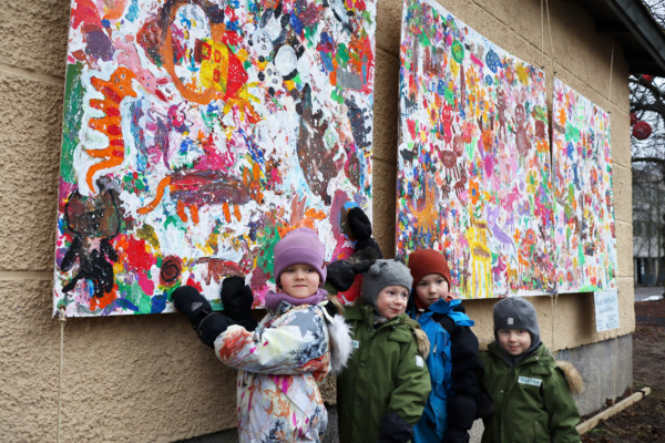 Fyra små barn i ytterkläder framför stora färggranna konstverk