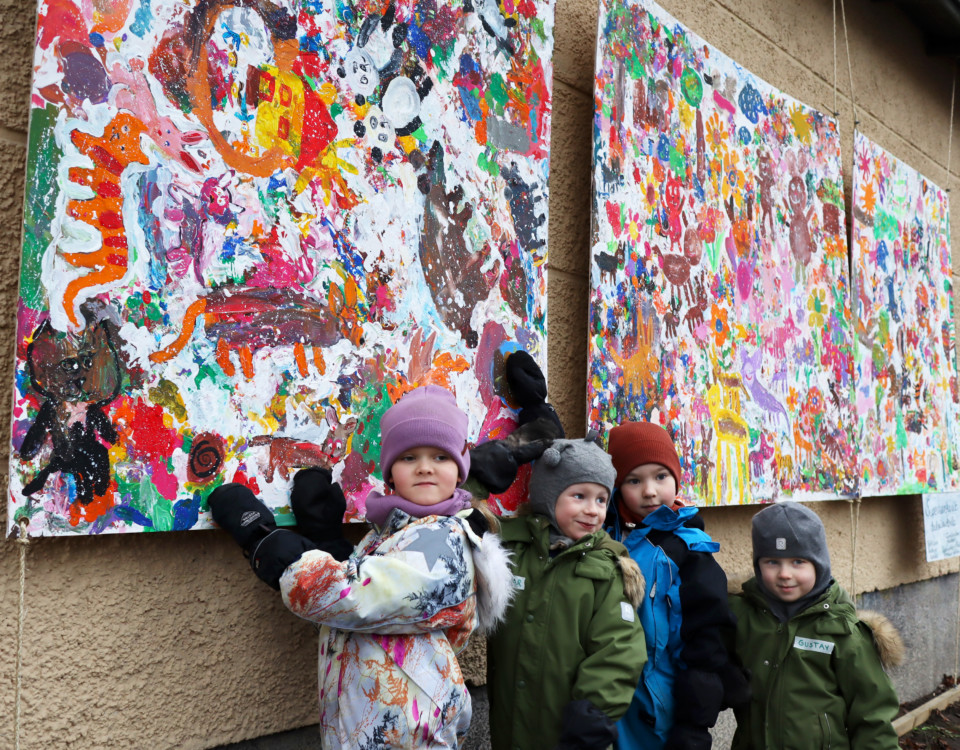 Fyra små barn i ytterkläder framför stora färggranna konstverk