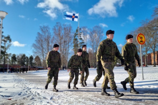 Sex unga militärklädda män som promenerar, Finlands flagga i bakgrunden