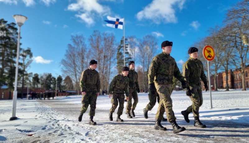 Sex unga militärklädda män som promenerar, Finlands flagga i bakgrunden