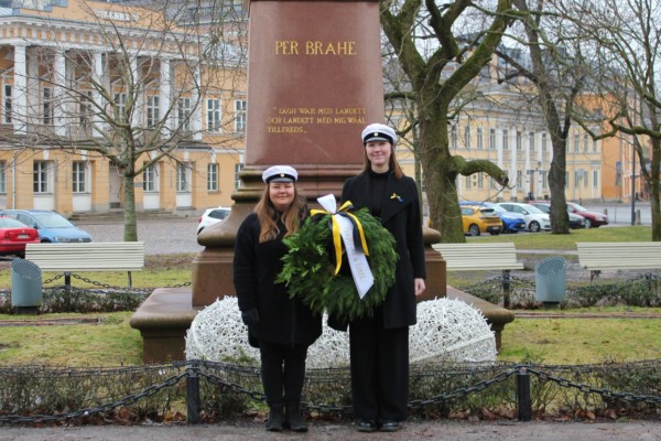 två unga kvinnor med studentmössor och stor krans vid staty