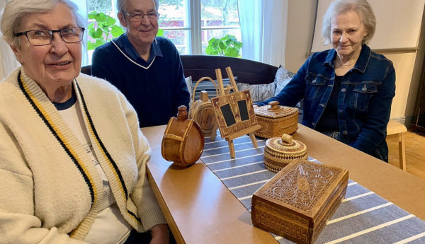 Tre seniorer sitter runt ett bord med gamla föremål