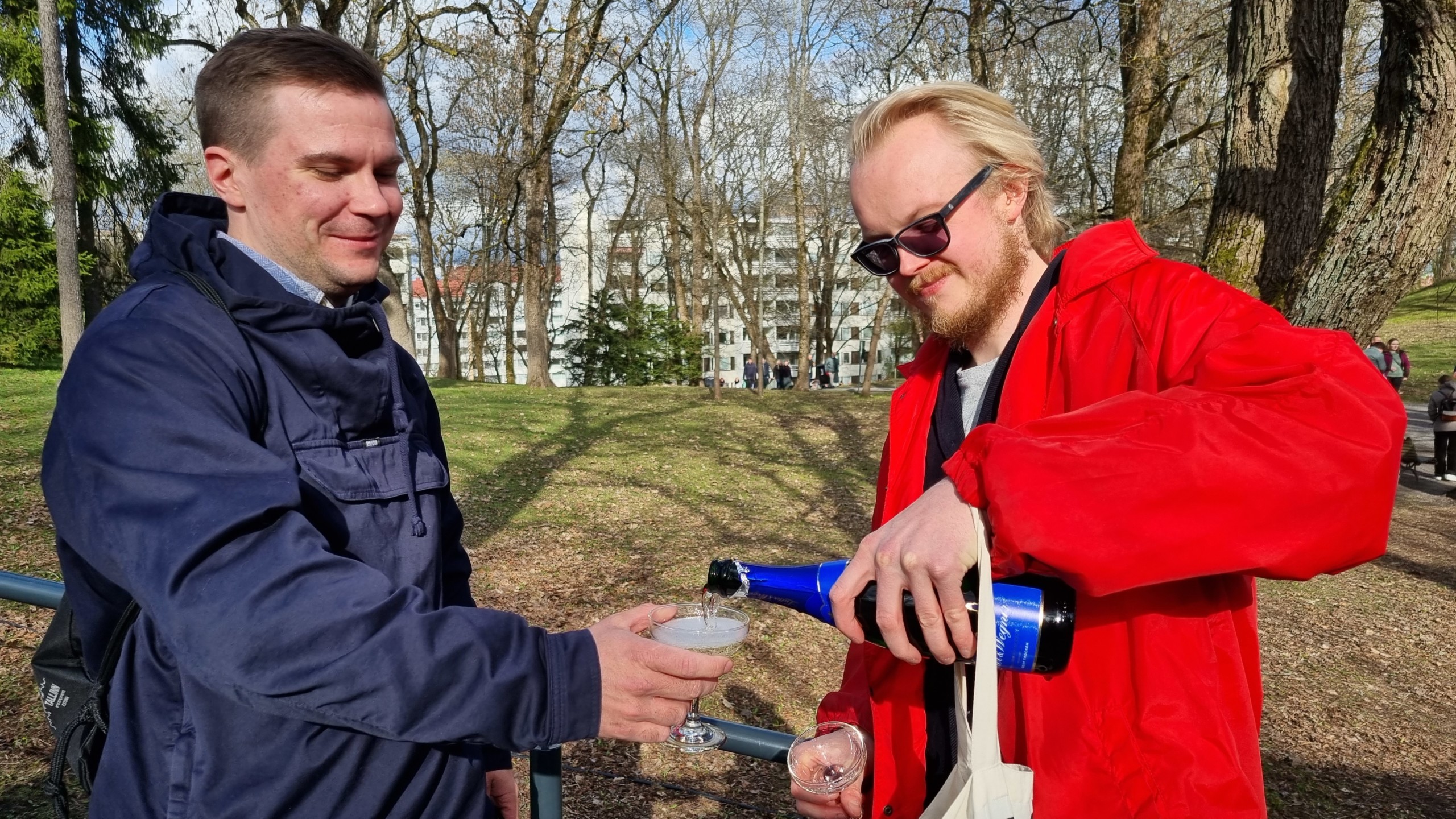 två män häller upp champagne i en park