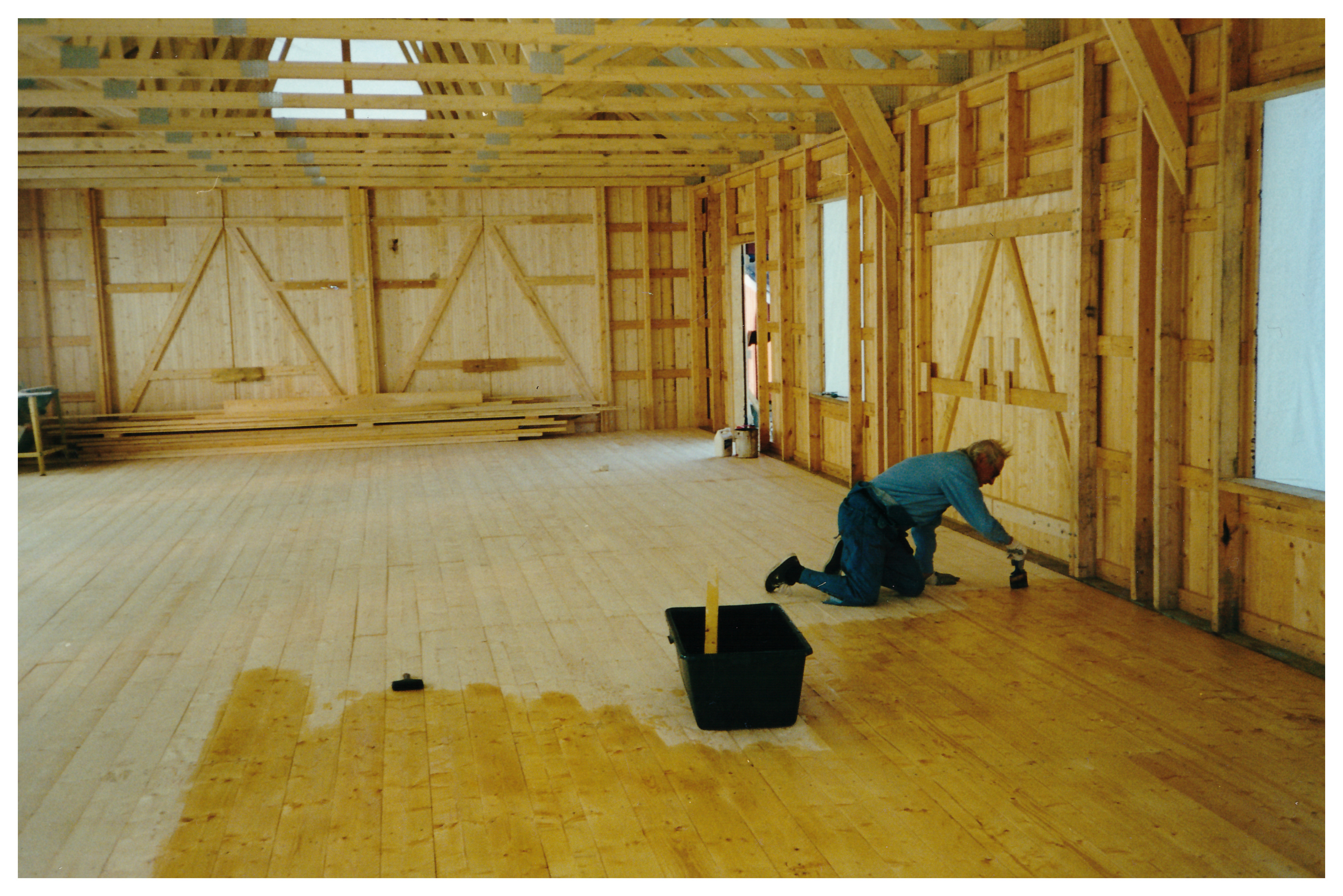 Ett stort rum i trä med en man på knä som målar golvet