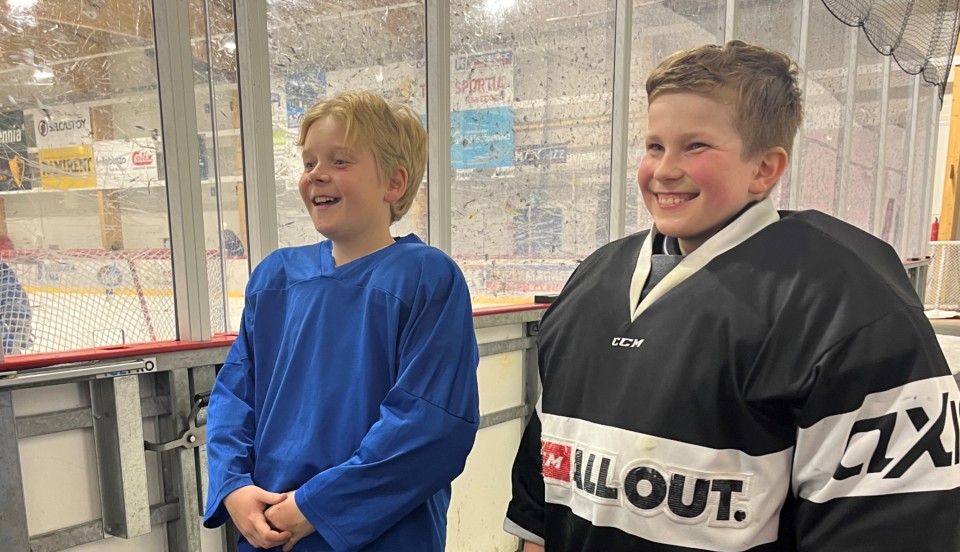 Två unga hockeyspelare ler vid sidan av rinken.