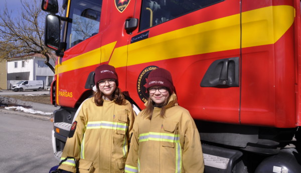 två flickor stpr framför en brandbil