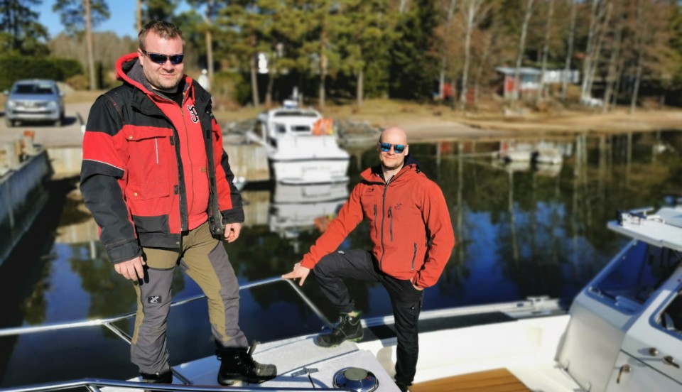 Två män på ett båtdäck framför en annan båt.