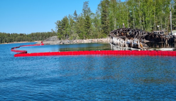 En sjunken gammal båt omringad av röda oljebommar