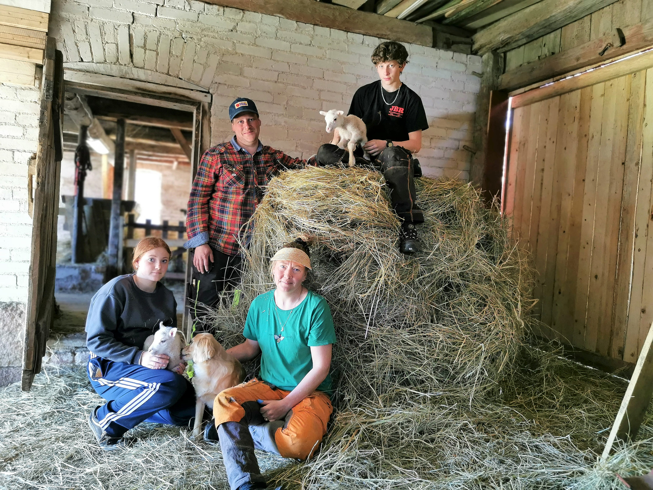 Fyra personer sitter på och kring en höbal i en ladugård.