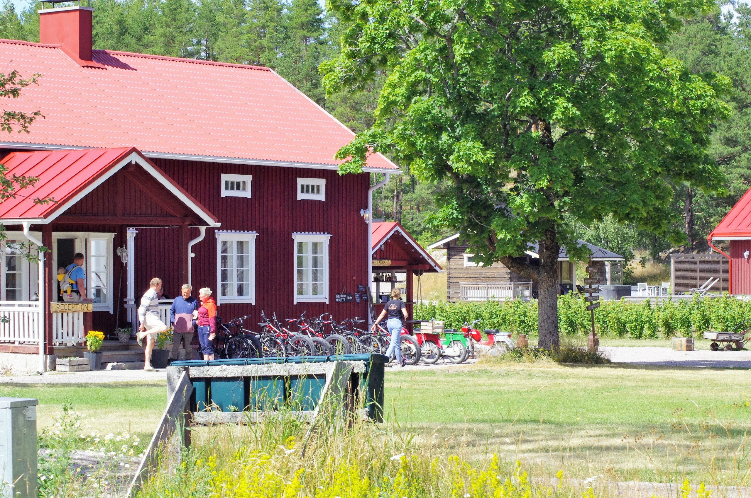 En gammaldags råd trähusbyggnad och gårdsplan med cyklar, människor och