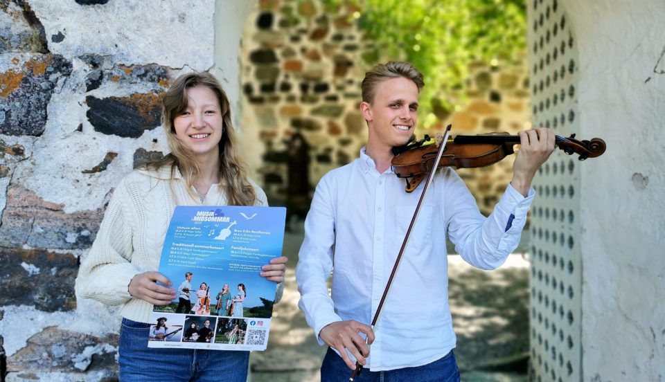 Kvinna som håller i affisch och man som spelar violin framför kyrka.