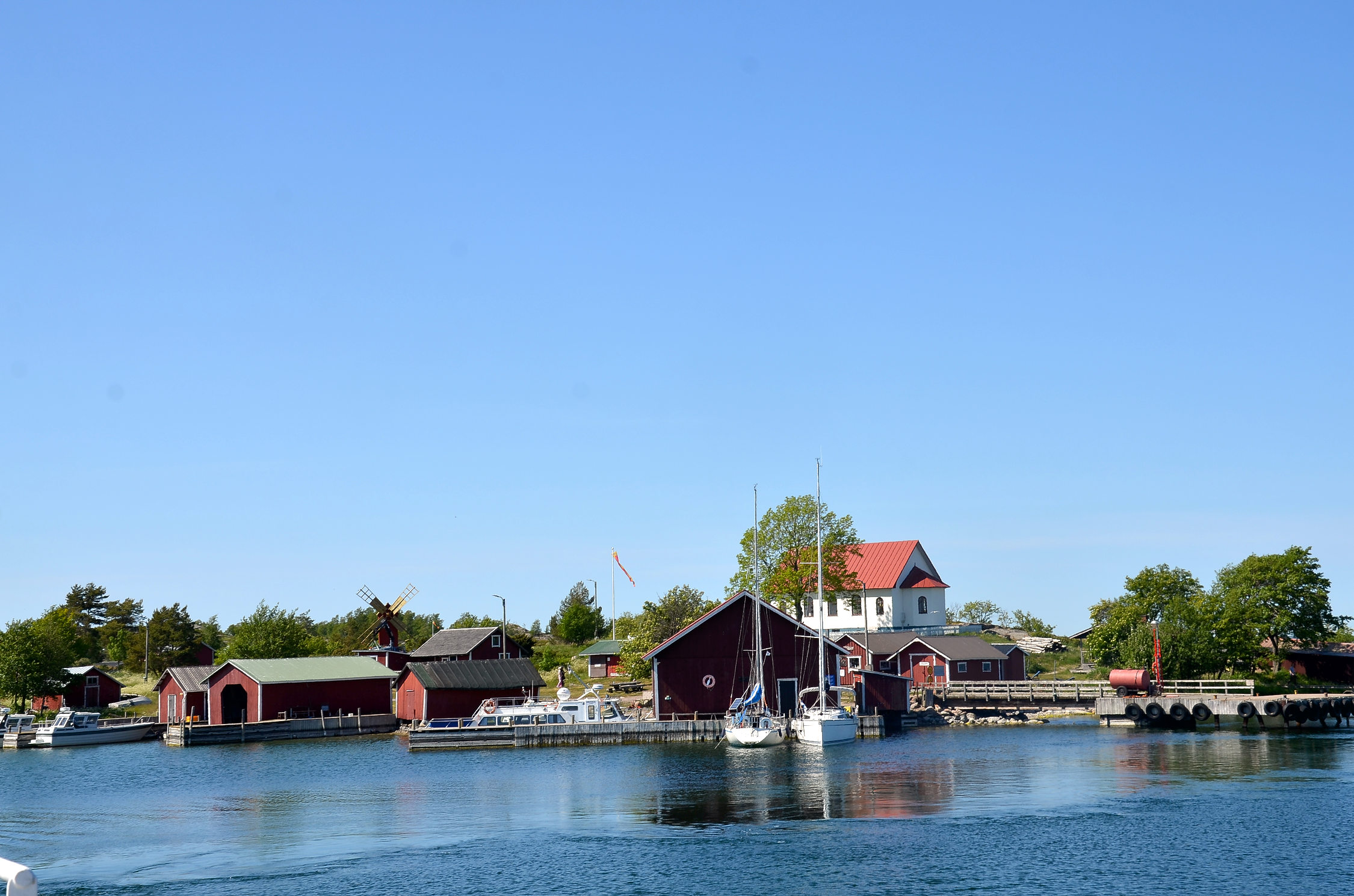 Röda hus, en väderkvarn, ett kapell och ett par segelbåtar på ön. Bilden är tagen från havet.