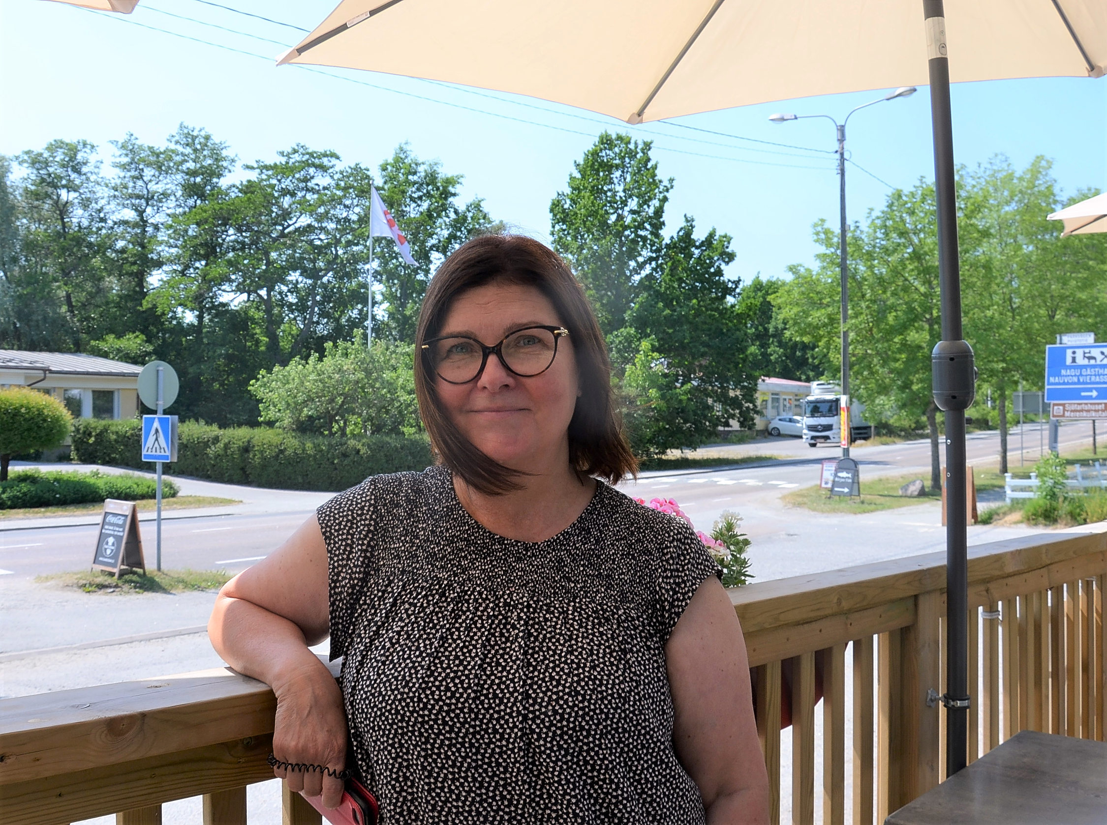 En kvinna med mörkt hår, glasögon och svart t-skjorta står på uteserveringen i restaurangen hon äger.