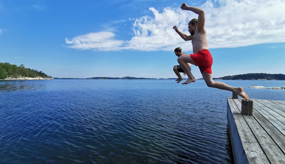 Två män som hoppar i havet från brygga