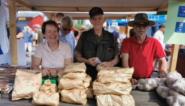 En kvinna och två män står bakom försäljningsbord med bruna påsar med potatis.