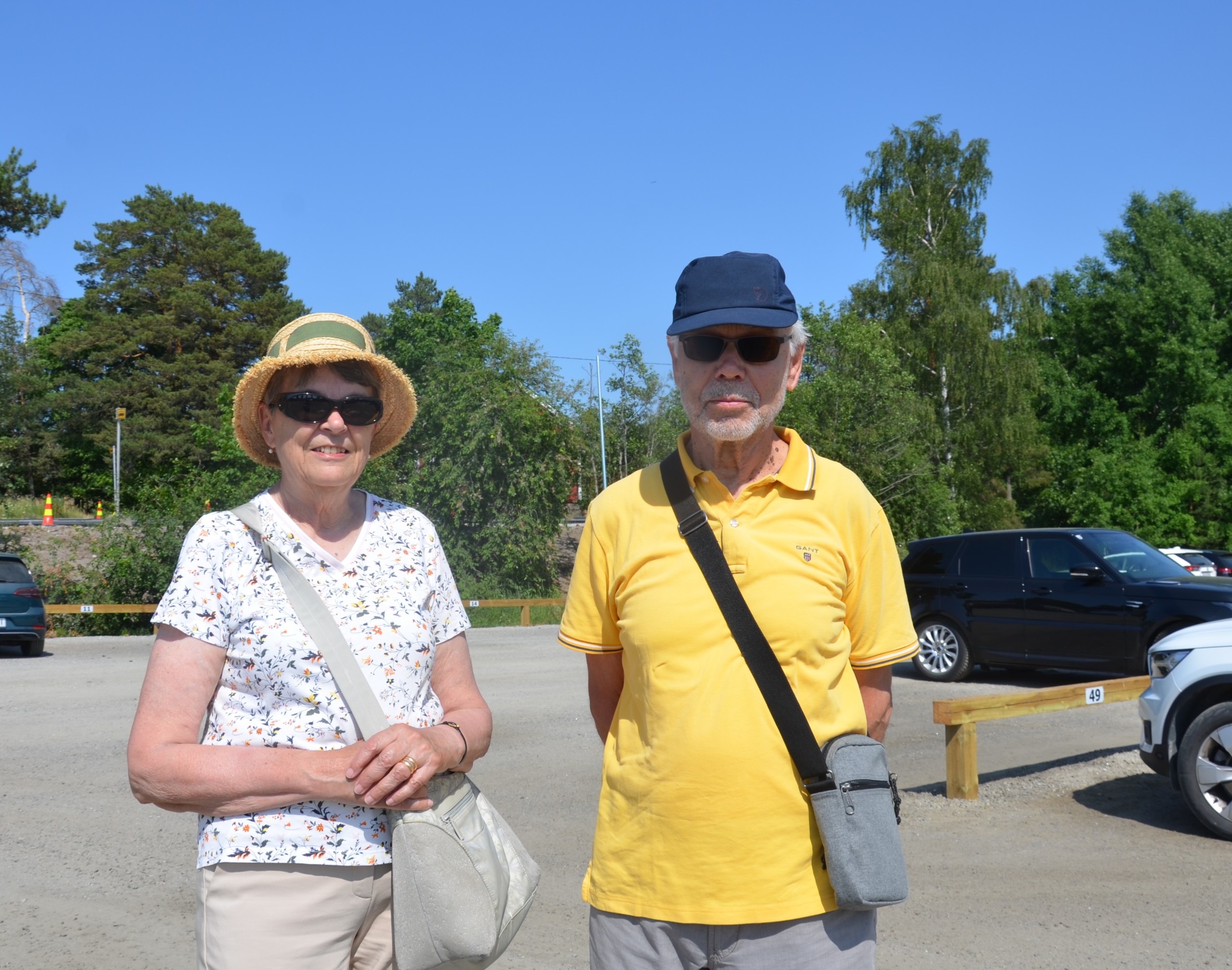 En kvinna och en man på parkeringsområdet i Nagu. Båda har hatt och solglasögon.