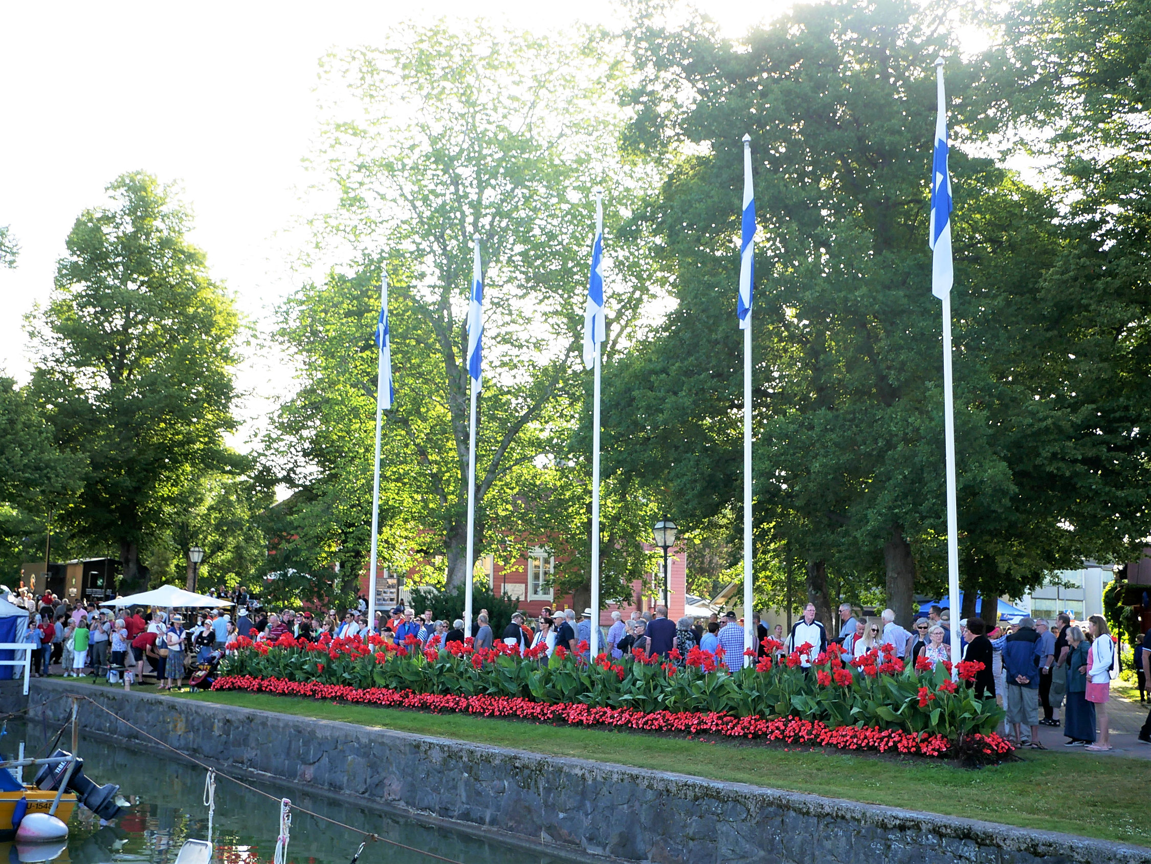 Massor av folk står invid fyra flaggor i Nådendal.