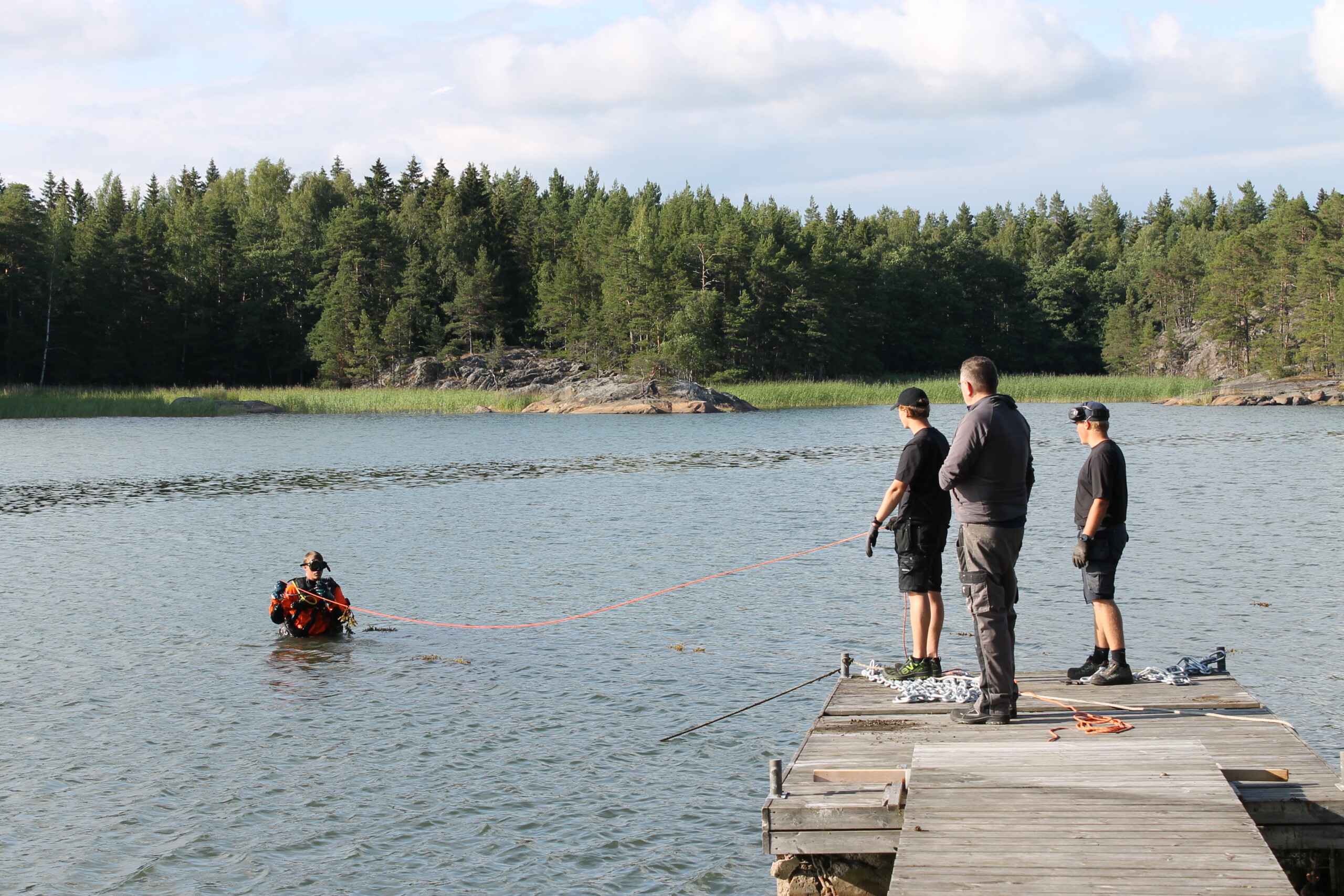 En dykare är i vattnet och tre män står på bryggan och följer med.