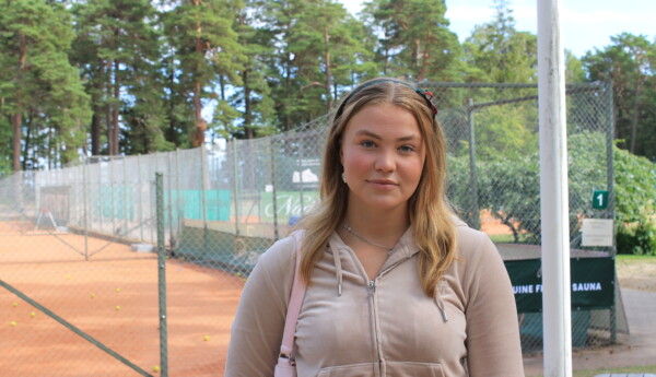 Ung kvinna står utomhus framför tennisbanor i Hangö.