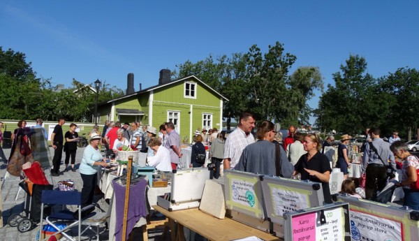 Solig dag på ett torg i Ekenäs med massa människor och loppisbord.