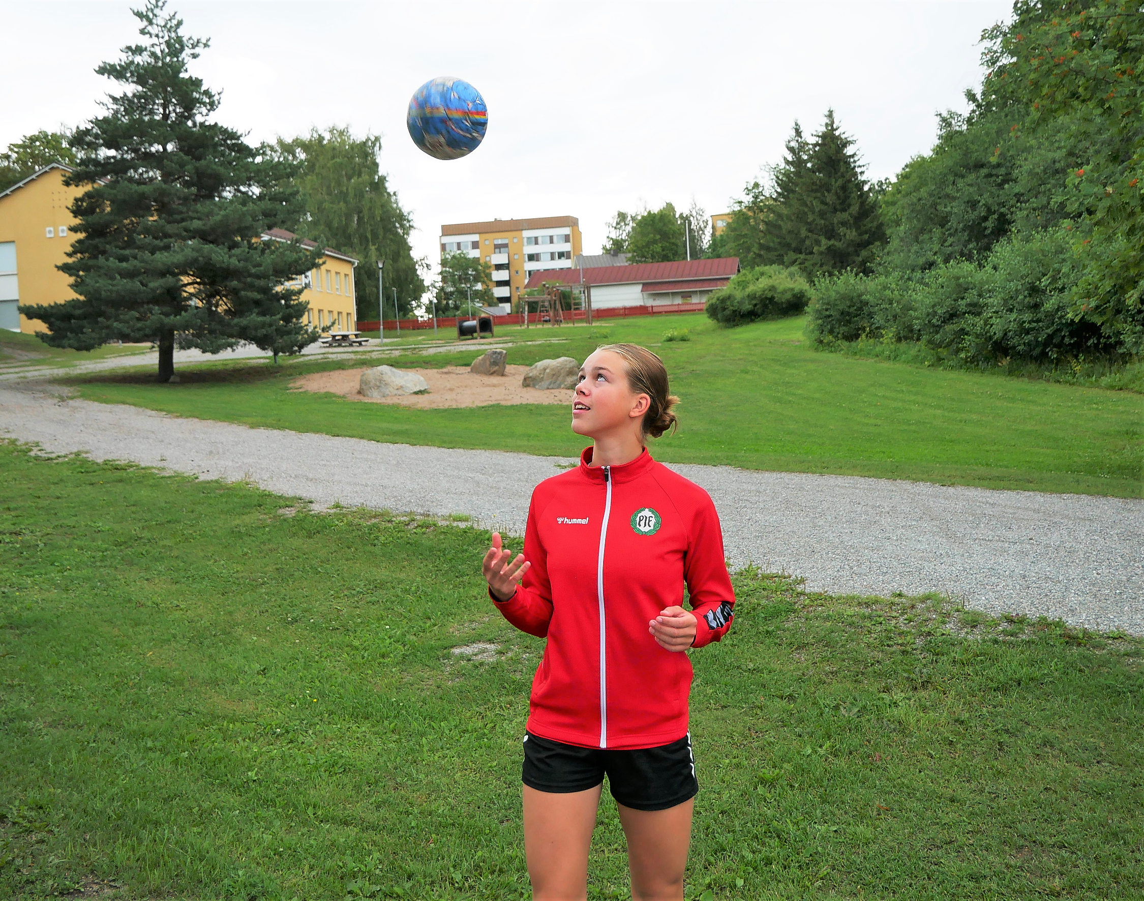 En flicka med röd långärmad slänger en handboll i luften.