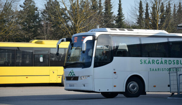 En vit buss står på en parkering framför en gul buss.
