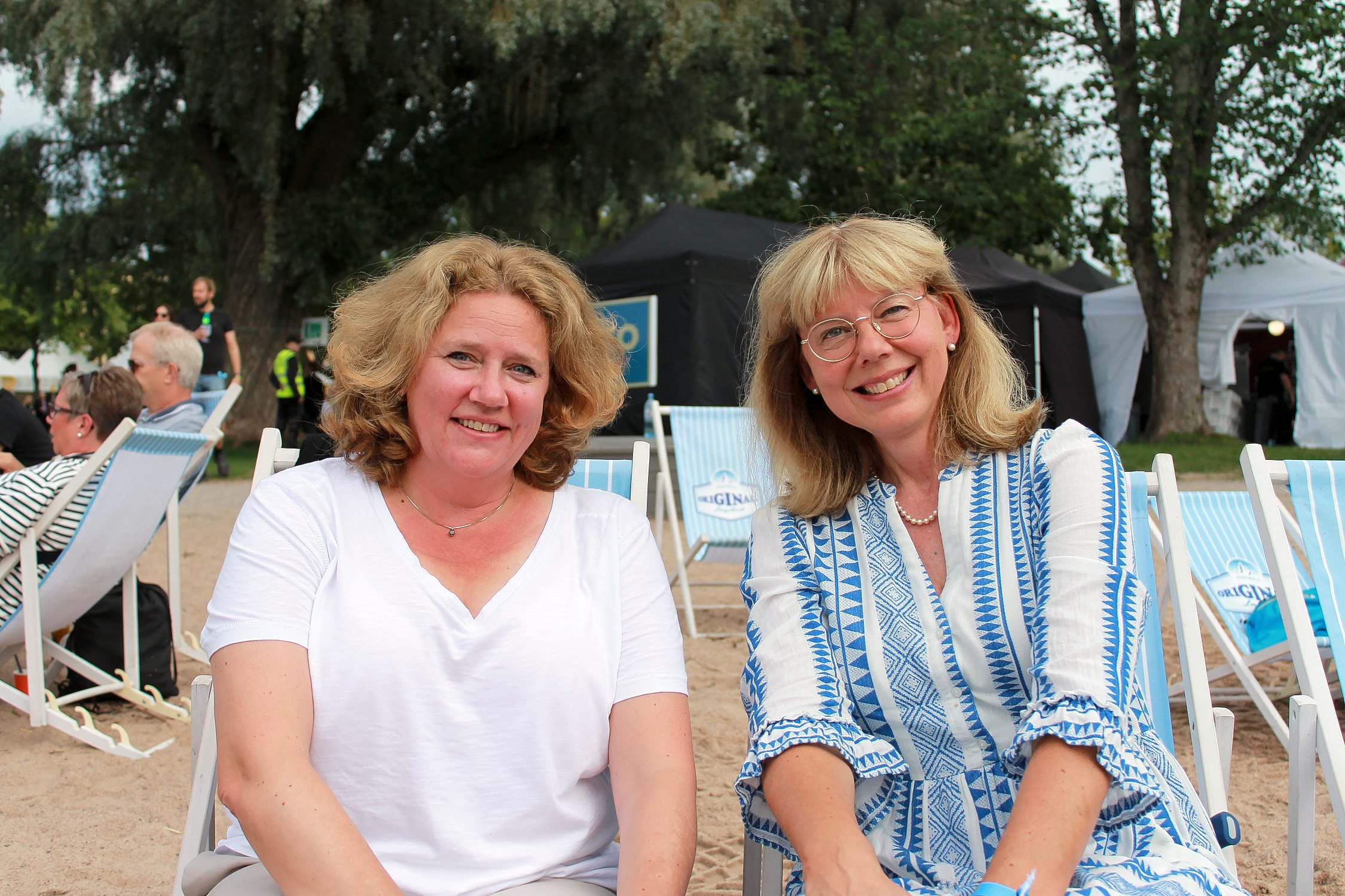 Två kvinnor sitter bredvid varandra och ler. De är besökare på Raseborgfestivalen i Stallörs parken, Ekenäs.