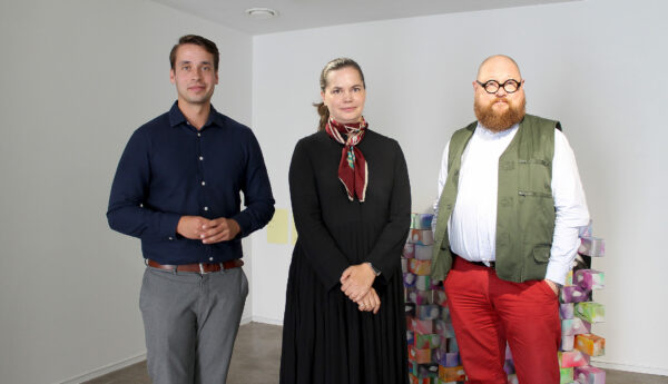 Tre människor, två män och en kvinna, står bredvid varandra och ler. De är på ett konstmuseum i Ekenäs.