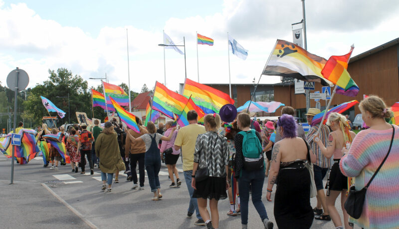 Prideparad i Karis under Raseborg Pride. Flera människor fotade då de går längs med en gata och flaggar regnbågsflaggor.