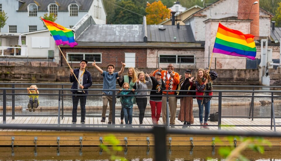 En grupp människor står på en bro och viftar med regnbågsflaggor och ser glada ut.