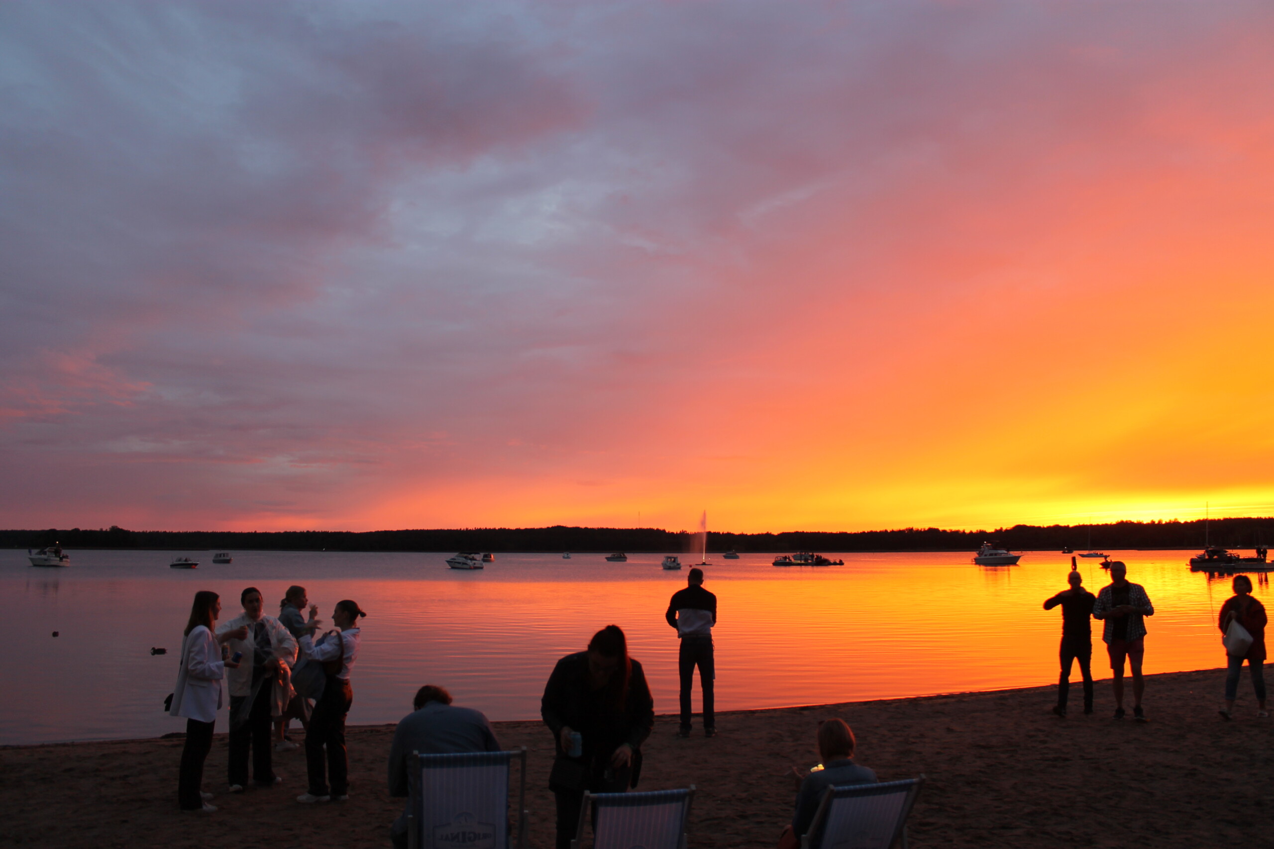 Bild över solnedgång på stranden i Stallörsparken, Ekenäs. Många människor på stranden och många båtar i vattnet.