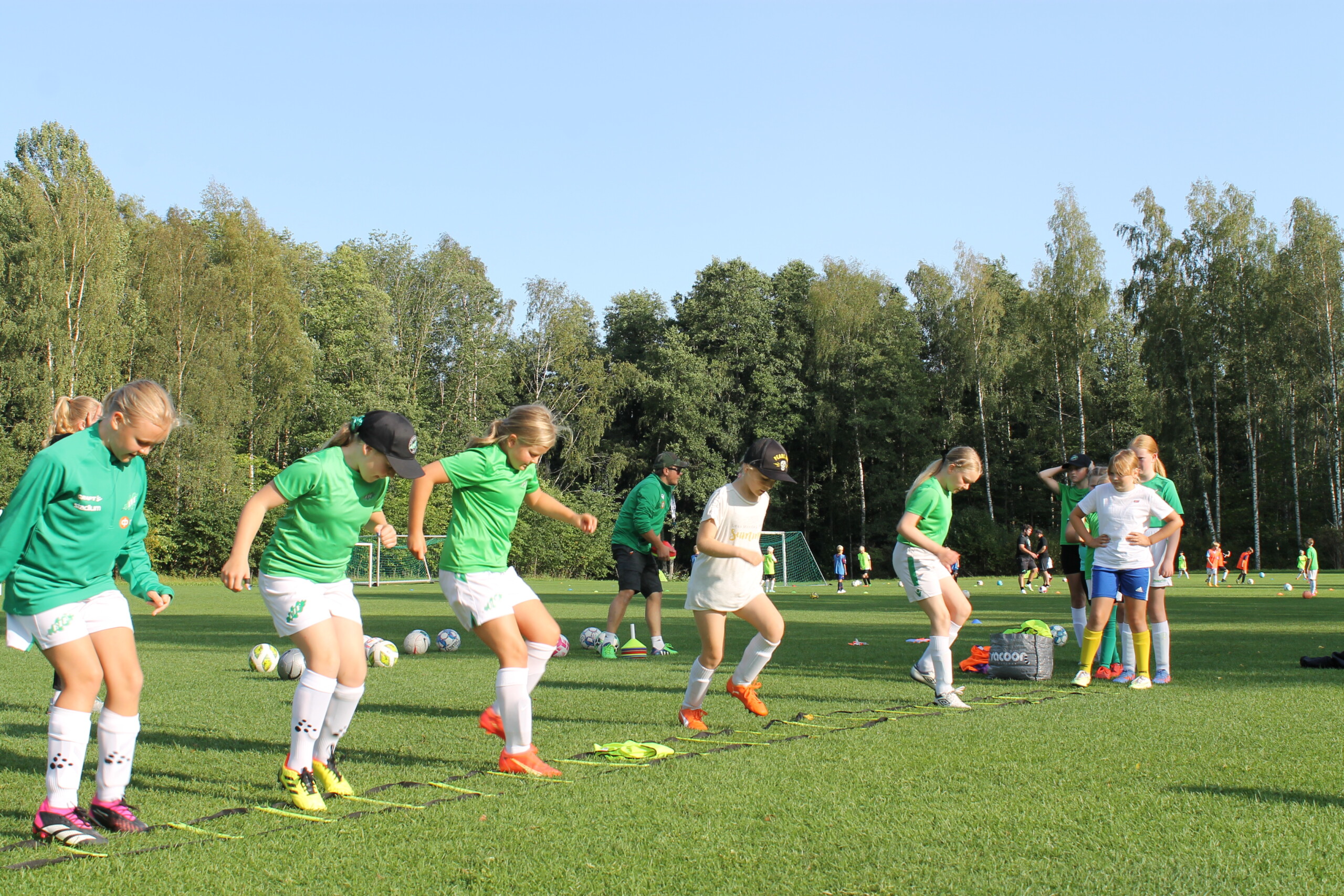 Flickor i åldrarna 12-13 som spelar fotboll i EIF. Flickorna står på rad och hoppar i olika mönster på en repstege som ligger på marken på gräsplanen där flickornas lag tränar.
